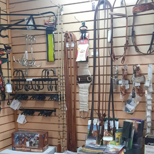 Wall display of horse tack in a store, featuring bridles, reins, stirrups, and a Western saddle box. The atmosphere is organized and rustic.